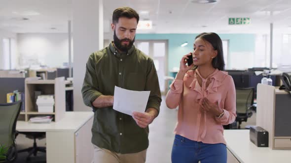 Video of diverse businesswoman and businessman using smartphone and walking in office