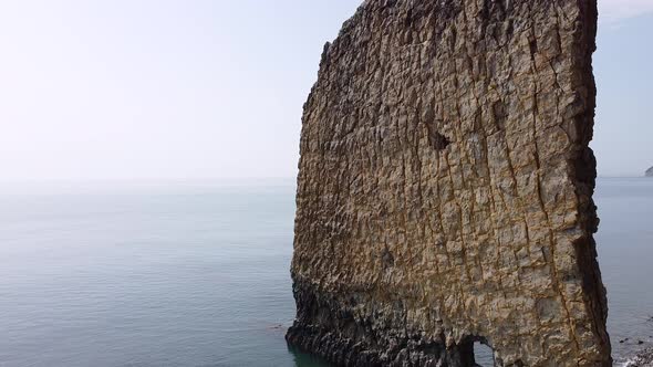 An unusual rock standing in the sea. Flat rock in the form of a sail with a hole in the middle