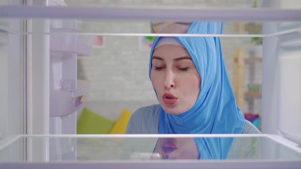 Young Muslim Woman in a National Headscarf Looks Into an Empty Refrigerator and Orders Food at Home