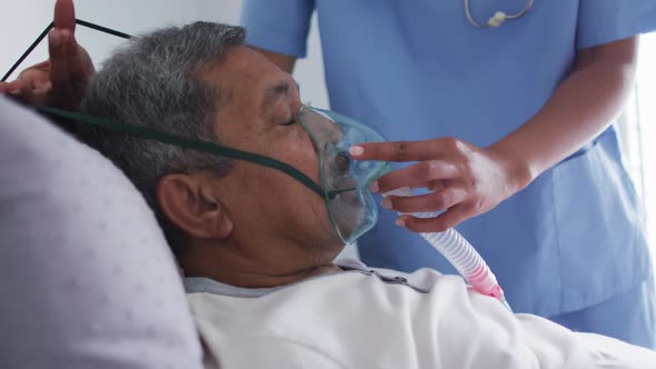 Mixed race female doctor assisting senior man in bed at home using ventilator