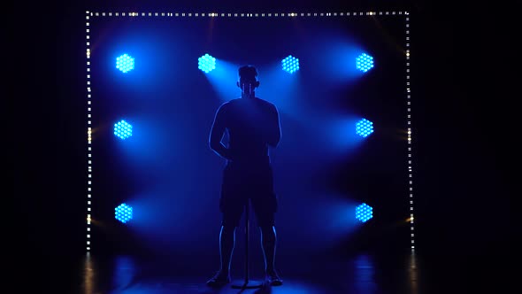 A Silhouette of a Guy in the Smoke Against the Background of Blue Lights Sings a Song Into a