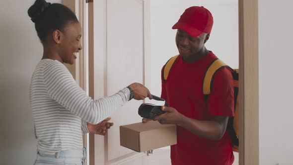 Young African American Woman Paying for Order with Smartphone and Getting Package Box From Postal