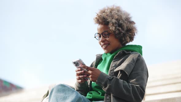 Pretty adult African woman wearing casual clothes typing on phone and looking around