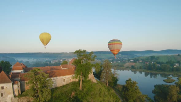 Colorful Hot Air Balloons Fly Over the Medieval Castle and Lake in the Morning Fog. Maneuverable