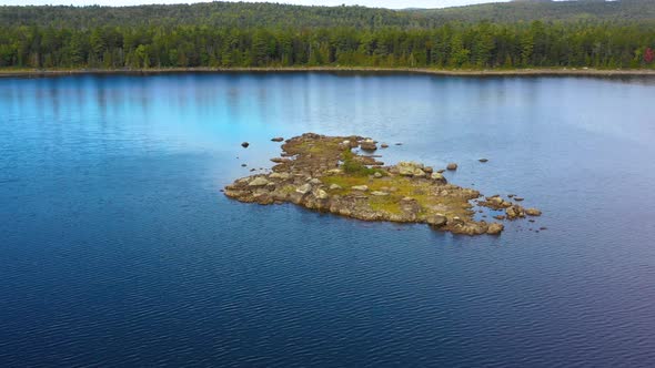 Early fall aerial footage of remote lake in northern Maine flying over small rocky island toward sho