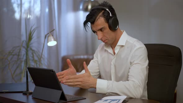 Serious Young Middle Eastern Businessman in Headphones Discussing Strategy with Colleagues in Video