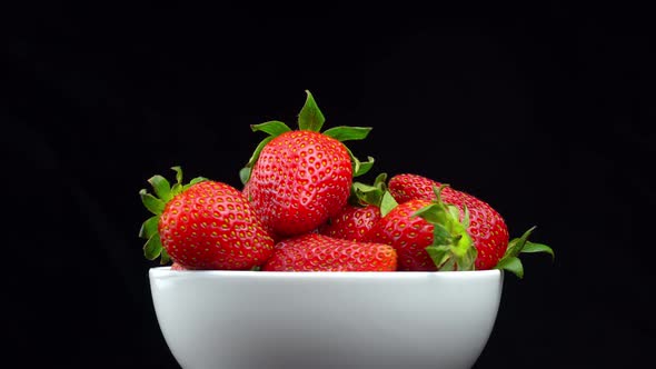 Appetizing strawberries with wilted green leaves lie on white porcelain bowl