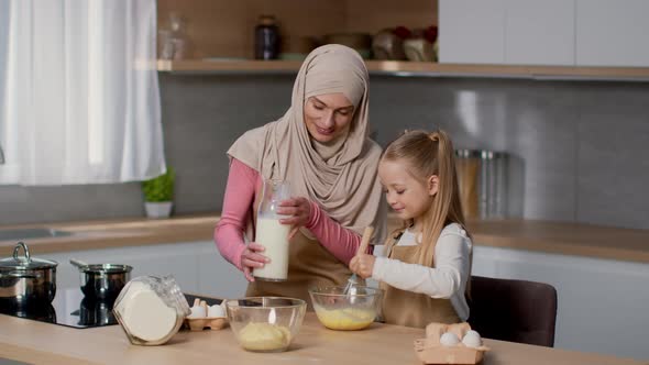 Cute Girl Helping Her Muslim Mother in Hijab to Cook Breakfast Whisking Eggs with Milk in Bowl and