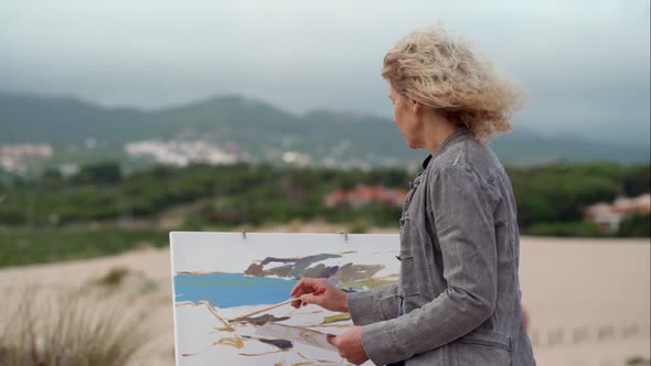 Middleaged European Woman Artist Paints a Seascape with an Original View of the Sea