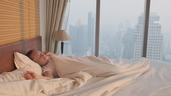 Woman waking up lying in bed on background of window 