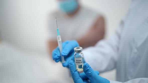 Closeup Covid19 Vaccine in Ampoule and Syringe in Nurse Hands with Blurred Unrecognizable Patient