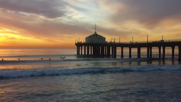 People Surfing Under the Manhattan Beach Pier at Sunset with a Lit Up Roundhouse Aquarium Roof in Ca