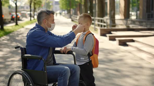 Disabled Father in Mask Sitting on the Wheel Chair Wearing Mask to His Son Before School Because of