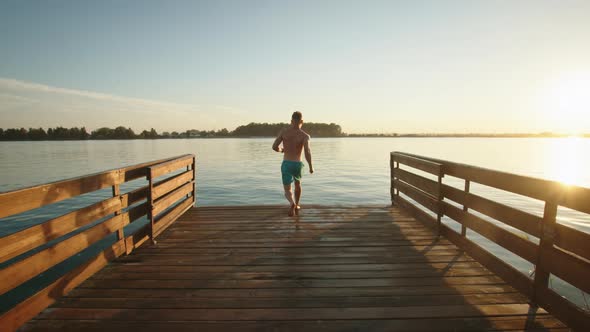 A Young Man is Running Down the Pier and Jumping Into the Lake in the Style of a Bomb