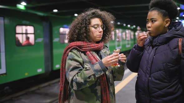 Two young multiethnic women in the underground eating snack