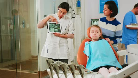 Doctor Holding Tablet with Xray Showing It To Mother of Girl Patient