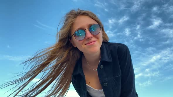 A Smiling Girl in Sunglasses on a Windy Bright Day, Close Up with the Blue Sky in the Back