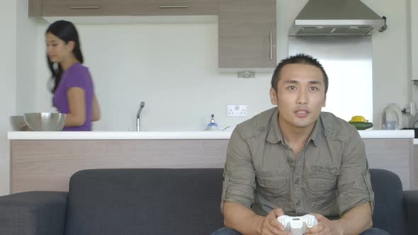 MS Young couple in kitchen man playing game and woman preparing food