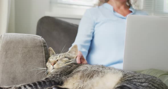 Senior caucasian woman wearing blue shirt and using laptop with cat in living room