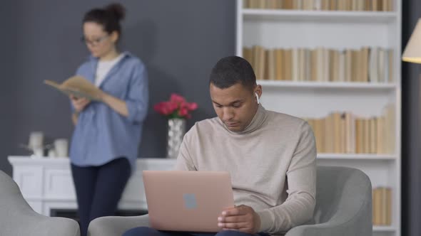 Young Handsome African American Man Opening Laptop Checking Email with Blurred Caucasian Woman