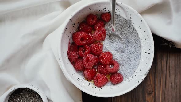 Close Up Shot of a White Bowl filled with Raspberries and Chia Seeds on a wooden table