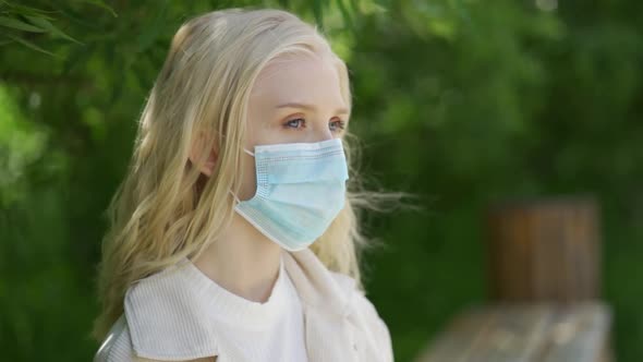 Sad Young Woman in a Medical Mask Sits in the Park