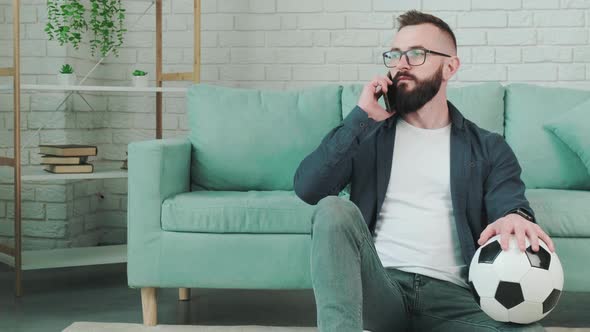 Man Standing with Soccer Ball in Hands and Talking on the Phone