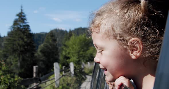 Happy Cute Little Girl with a Smile Stuck Out of the Car Window Into the Wind. Slow Motion