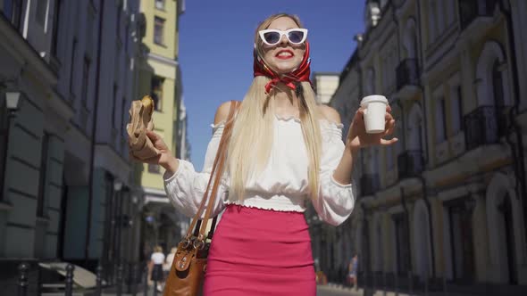 Beautiful Young Woman Walking on the Street Drinking Coffee and Eating Croissant. Attractive