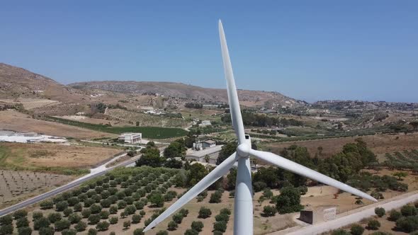 Aerial: wind turbine turning on mediterranean hillside, closeup reveal