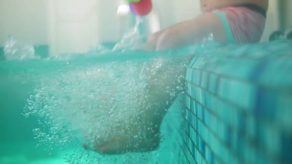 Playful Toddler Sitting on the Pool Edge Splashing the Water While Kicking His Legs in the Water