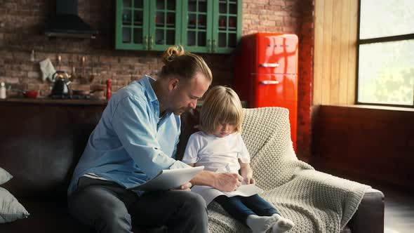 Young Dad in Casual Outfit is Helping His Kid to Do Homework in School Copybook