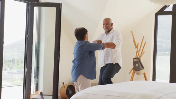 Happy senior diverse couple dancing in living room at retirement home