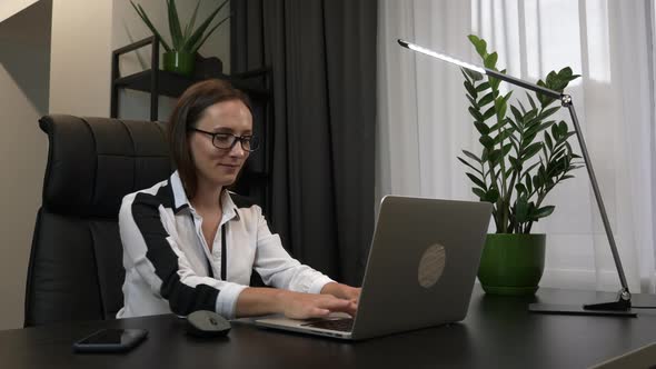 Businesswoman in eyeglasses is opening laptop computer and starting to work at modern home office