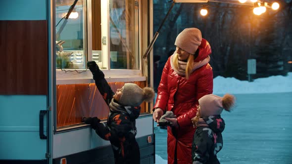 A Young Woman Mother with Her Children Standing Near a Little Shop Near the Ice Rink