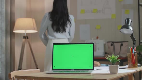 Green Screen Laptop Is On The Table While A Woman Walks Into Looking At The Sketch Paper On The Wall