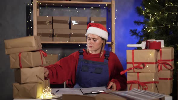 Small Business Worker in Santa Claus Costume Marks Goods in Warehouse Counts Boxes Finds Crumpled