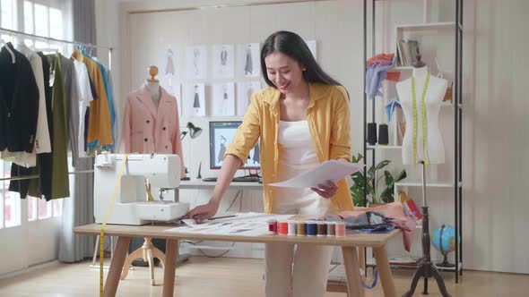 Female Designer With Sewing Machine Rearranging And Looking At The Papers While Designing Clothes