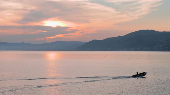 Dinghy moving from left to right at sunset, with mountains in the background and orange sky, shot ne