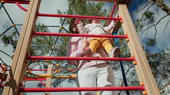 A little pretty child climbs the children's sports wall with the help of his mother.