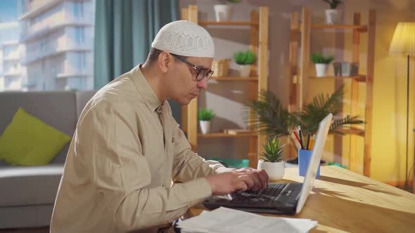 Muslim in a Skullcap Works at Home on a Laptop
