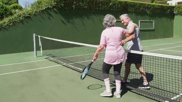 Happy caucasian senior couple embracing over the net at outdoor tennis court after playing a game