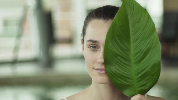 Young woman holding large leaf in front of her face, portrait