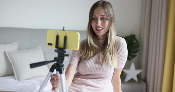 Happy Young Caucasian Woman with Blonde Hair Holding Tripod with Mobile Phone and Communicating with