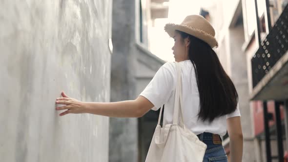 Asian woman wears a vintage hat and holding a Cloth bag and uses her hands to touch softly wall.