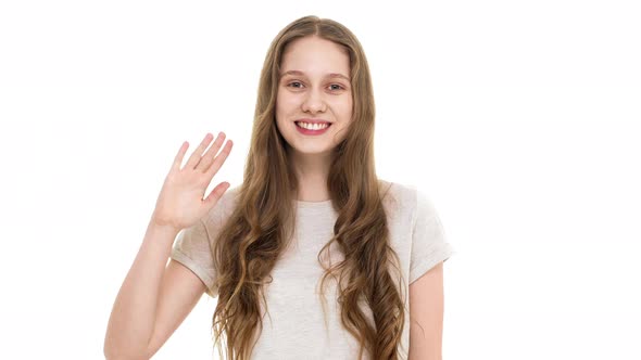 Portrait of Friendly Young Female with Pleasant Appearance Smiling on Camera and Waving Hand Like