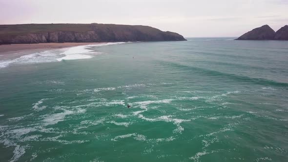 Surfer swims laterally across waves. Drone-shot. Holywell Bay, Newquay, Cornwall.