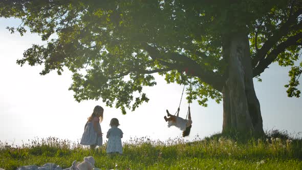 Two Sisters Run Across Clean Green Field To Their Mother, Swinging on Swing Tied To an Old Oak-tree.