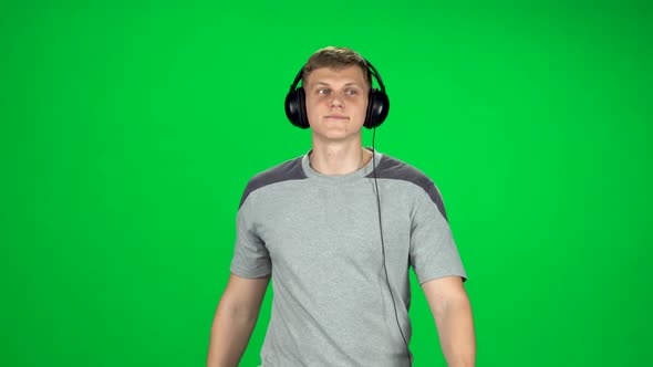 Man in Big Headphones Goes, Listening Music and Dancing on Green Screen at Studio