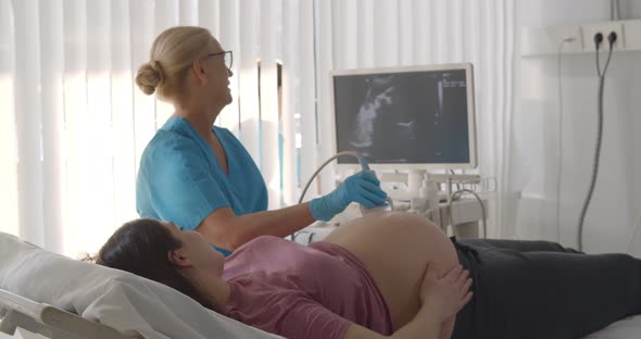 Senior Doctor Doing Ultrasound Scan for Young Pregnant Woman in Hospital